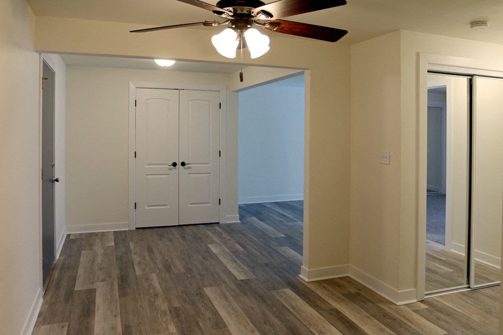 an empty living room with a ceiling fan and a mirrored closet