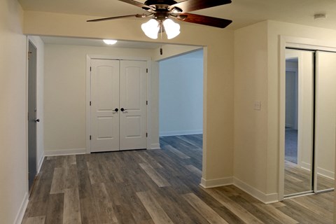 an empty living room with a ceiling fan and a mirrored closet