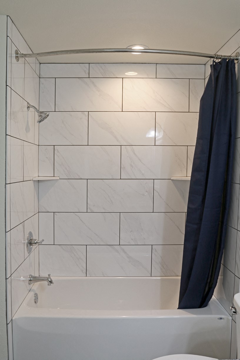 the shower has a blue shower curtain and a white tiled bathroom with a tub