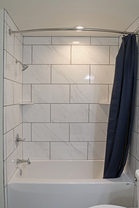 the shower has a blue shower curtain and a white tiled bathroom with a tub