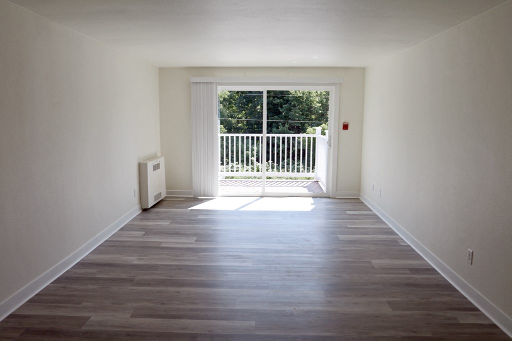 an empty living room with wooden floors and a door to a balcony