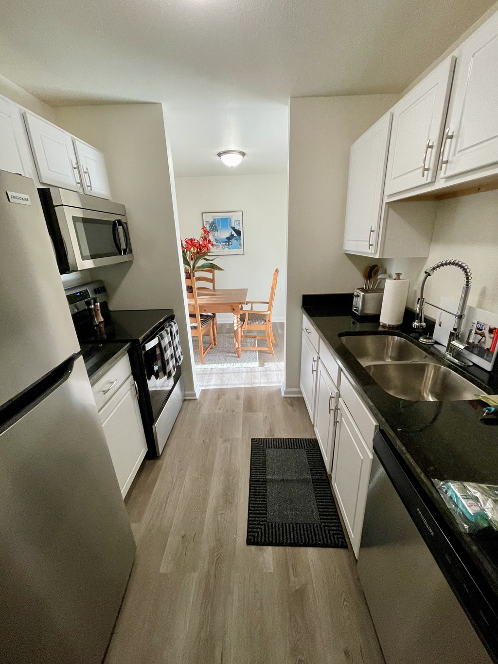 A kitchen with a stainless steel refrigerator and black countertops.