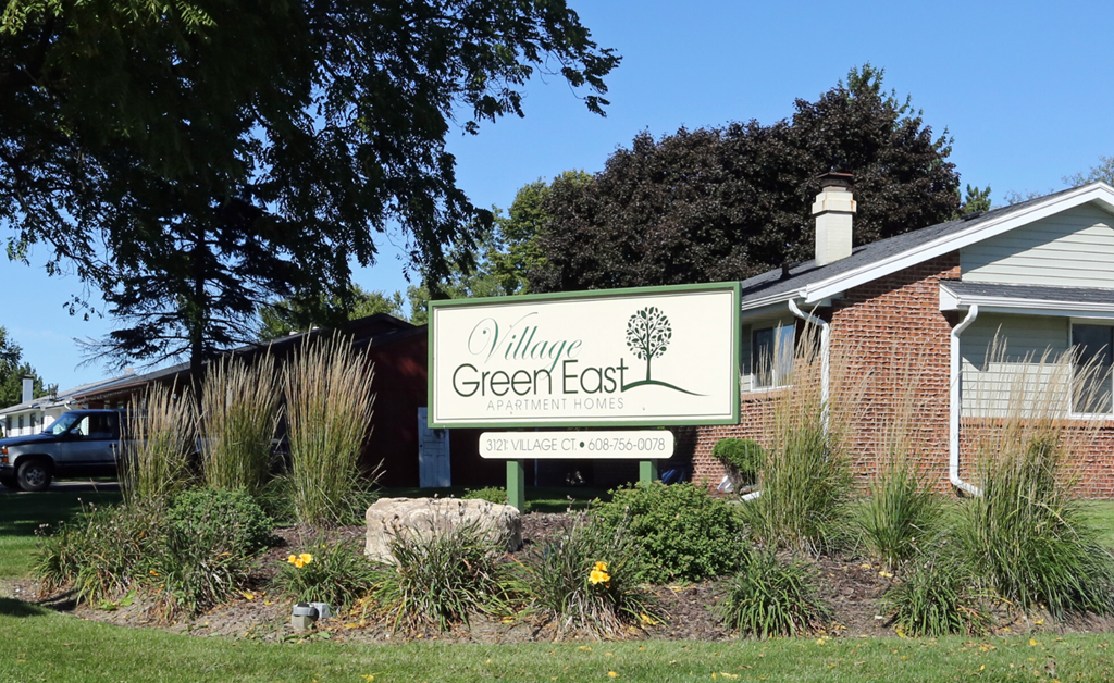 A sign for the GreenEast Village is displayed in front of a building.