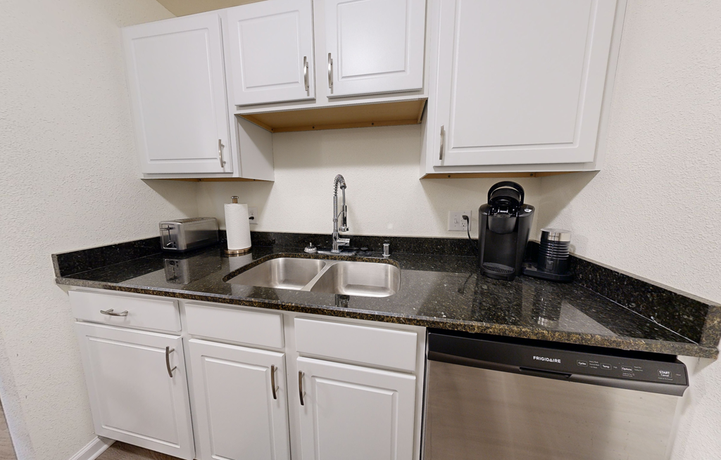 A kitchen with white cabinets and a black granite countertop.