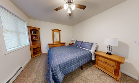 A bedroom with a bed, nightstand, and a window with blinds.