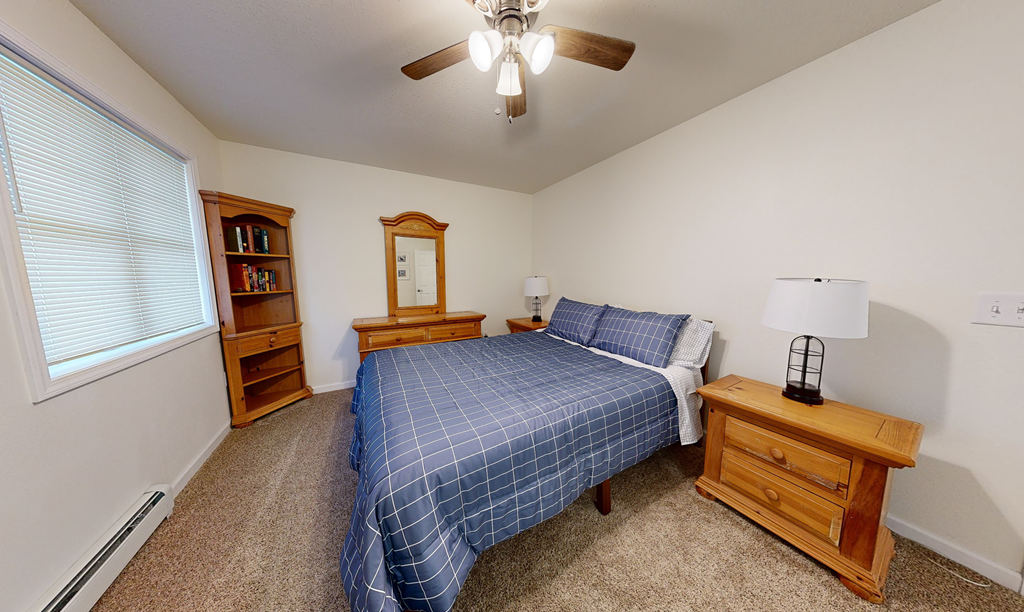 A bedroom with a bed, nightstand, and a window with blinds.