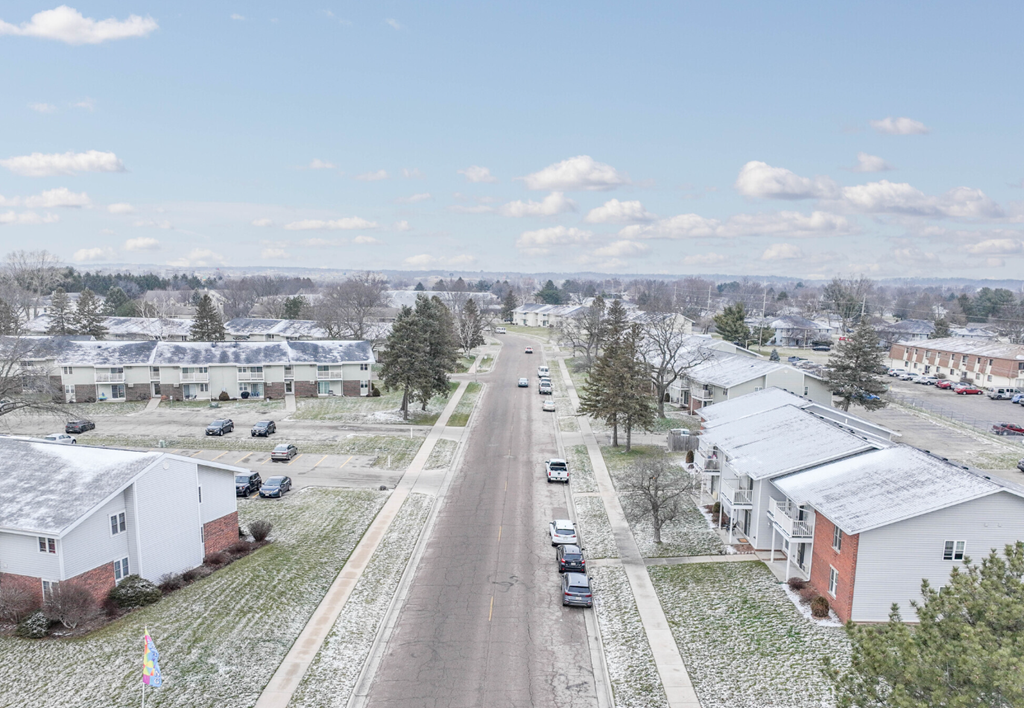 A street view of a residential area with houses on both sides and cars parked along the road.