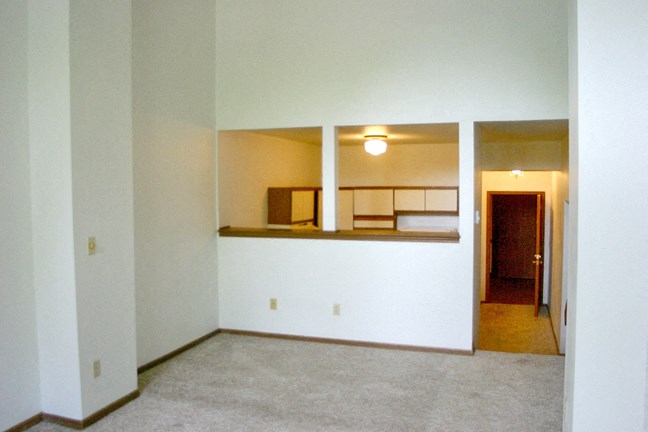 an empty living room with white walls and a kitchen