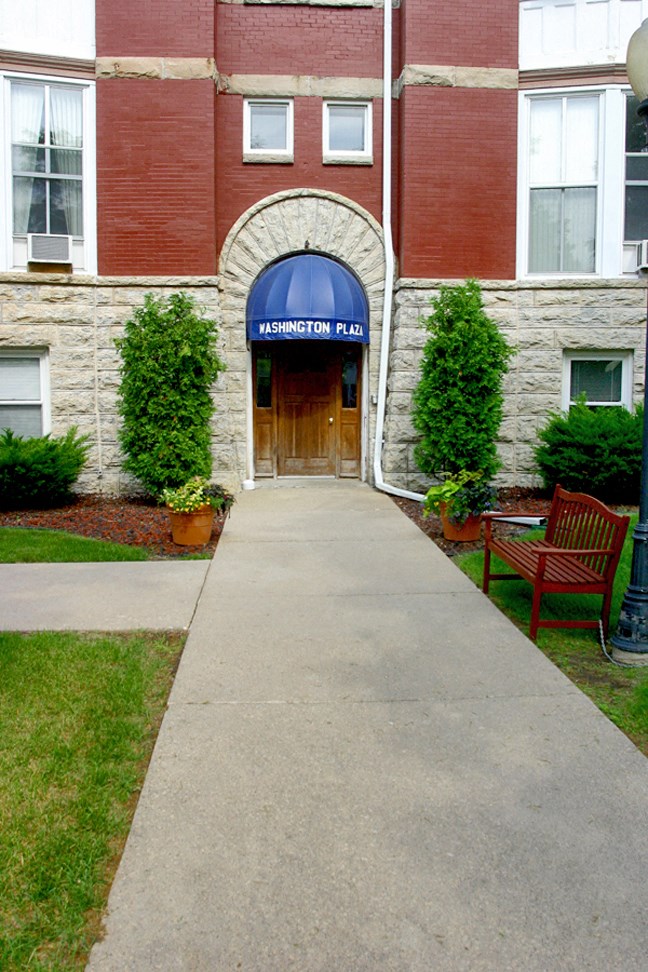 a walkway in front of a brick building with a blue sign on the door