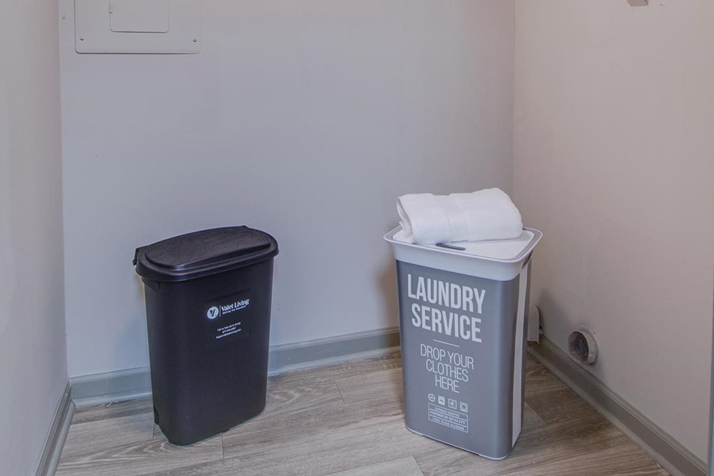 a bathroom with a trash can and a laundry service bucket