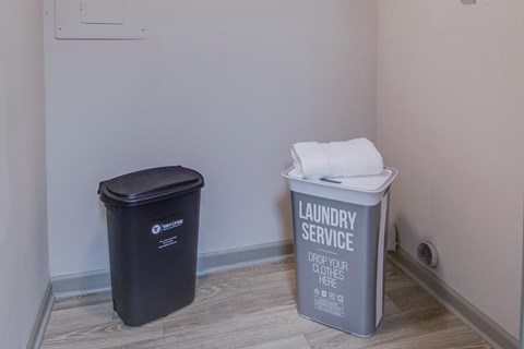 a bathroom with a trash can and a laundry service bucket