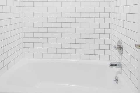 a white bath tub in a white tiled bathroom