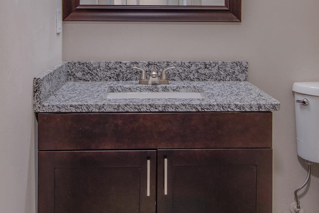a bathroom sink with granite counter top and a mirror