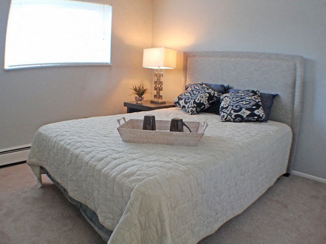 a bedroom with a bed, nightstand, and a window  at Valley York Apartments, Parma Heights, OH