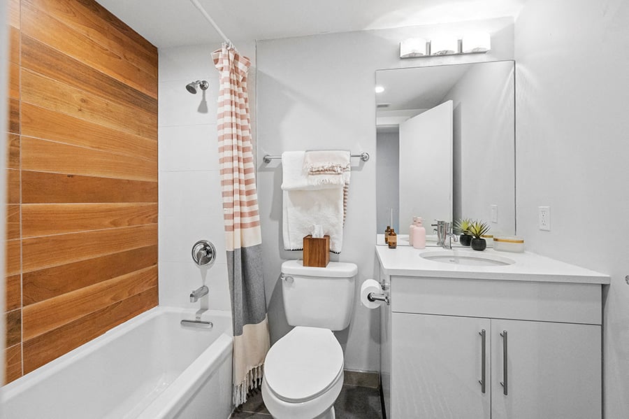 Contemporary tiled shower and white sink and vanity in renovated student apartment bathroom