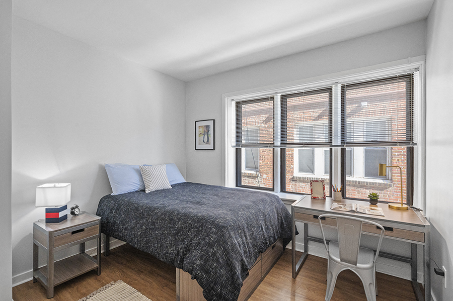 Spacious student apartment bedroom furnished with full size bed, large desk, and bedside table