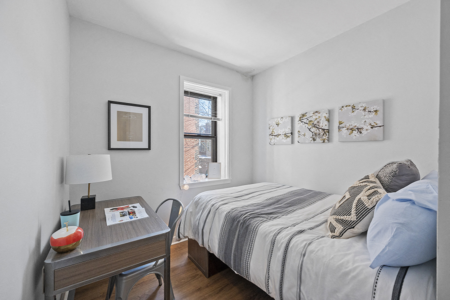 Student apartment bedroom furnished with desk and twin sized bed in front of sunny window