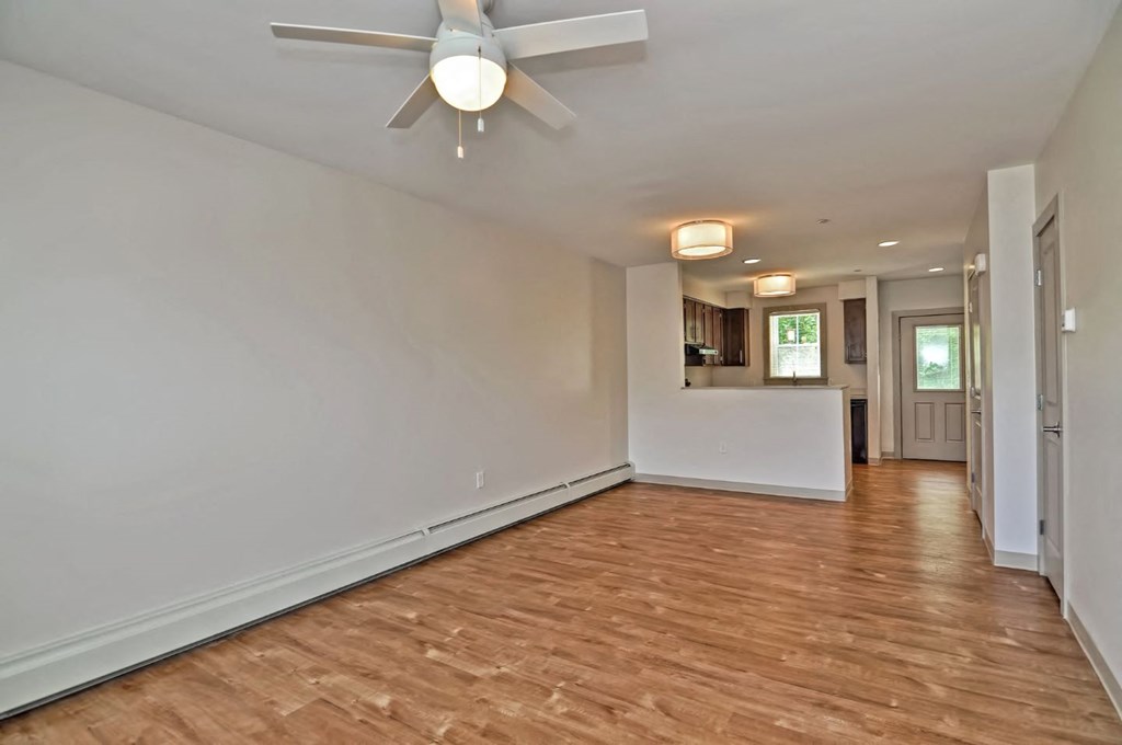 an empty living room with a ceiling fan and a kitchen