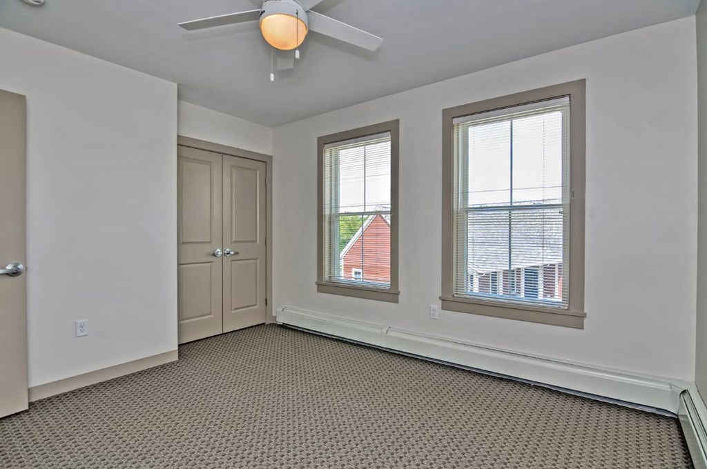 an empty living room with two windows and a ceiling fan