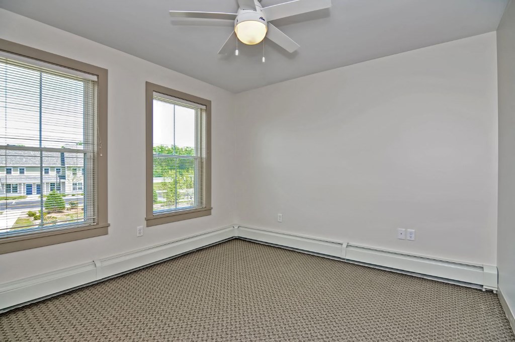 an empty living room with a ceiling fan and two windows