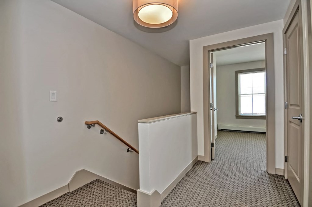 the landing of a staircase in a home with a door to a hallway with stairs