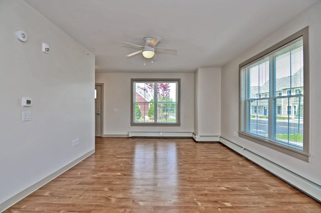 an empty living room with a large window and a ceiling fan