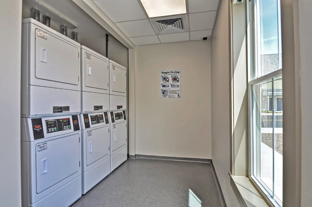 a room with a row of white washers and dryers and a window