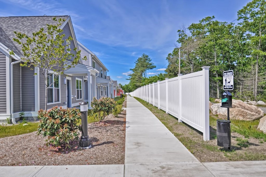 a sidewalk in front of a house with a white fence