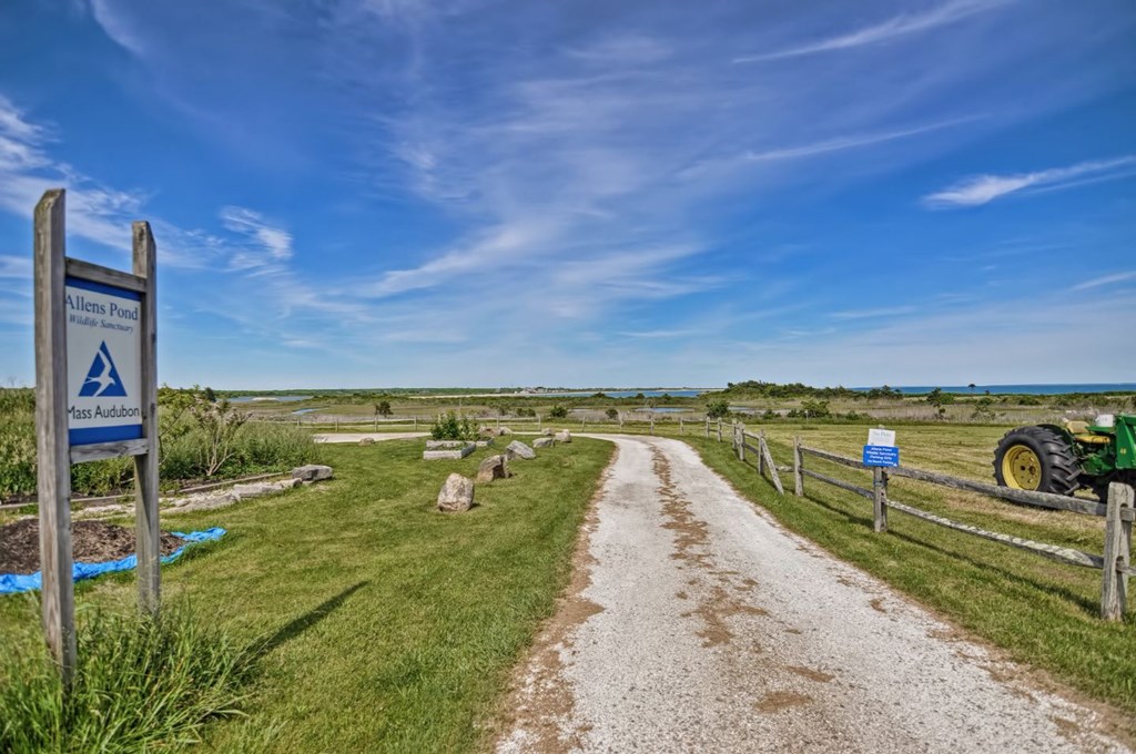 a dirt road leading to a farm with a sign next to it