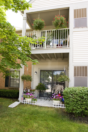 the front of the house has a balcony and a yard with potted plants