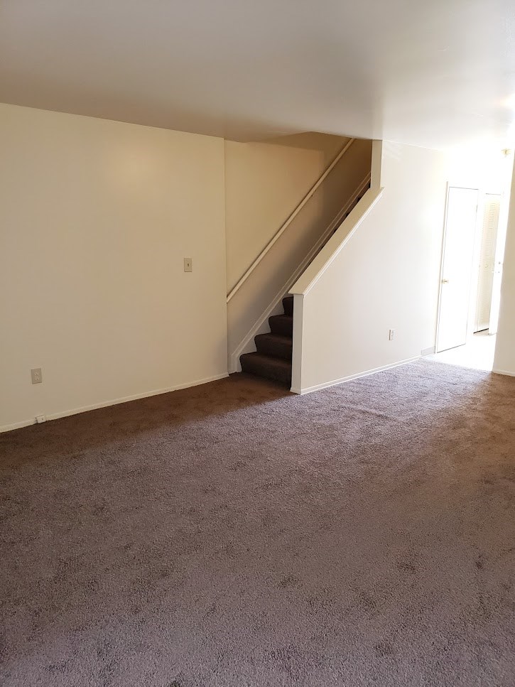 an empty living room with a carpeted floor and stairs