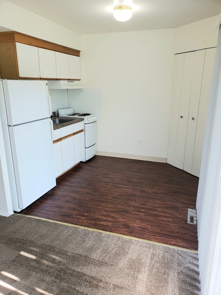 an empty kitchen with white appliances and a wood floor