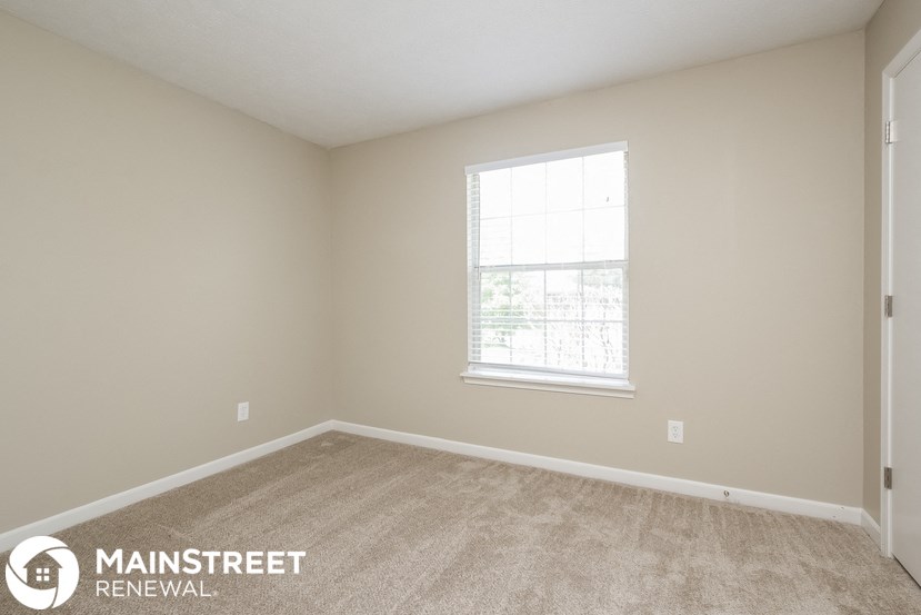 the upstairs bedroom has a large window and beige carpeting