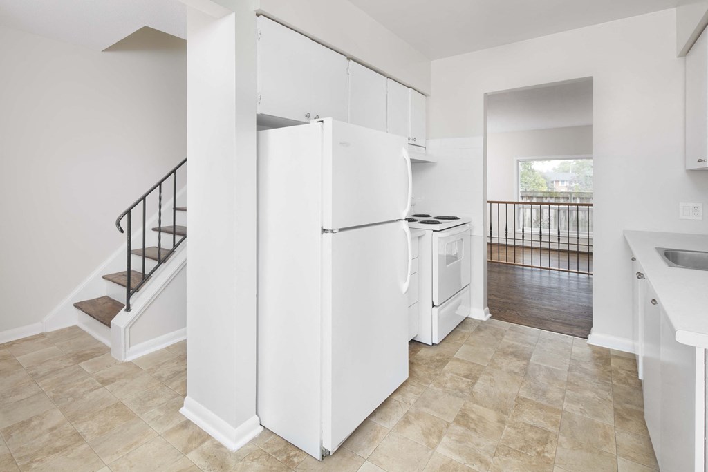 a white kitchen with a white refrigerator and a staircase
