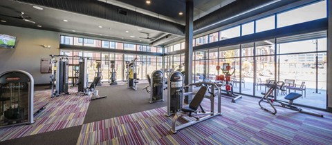 a gym with weights and cardio equipment in a building with large windows