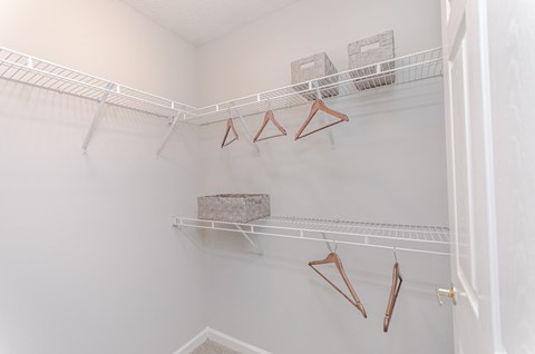 a walk in closet with white walls and a white closet shelf with hooks