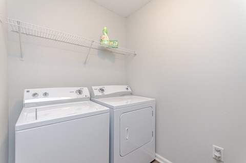 a white washer and dryer in a white room with a shelf above them