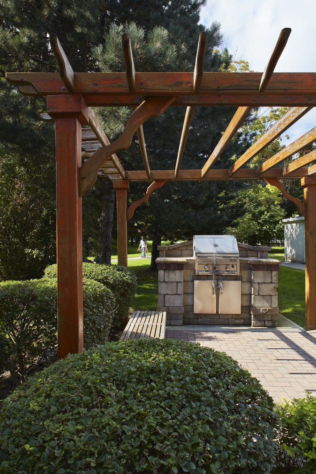 a stone grill is under a wooden pergola in a garden