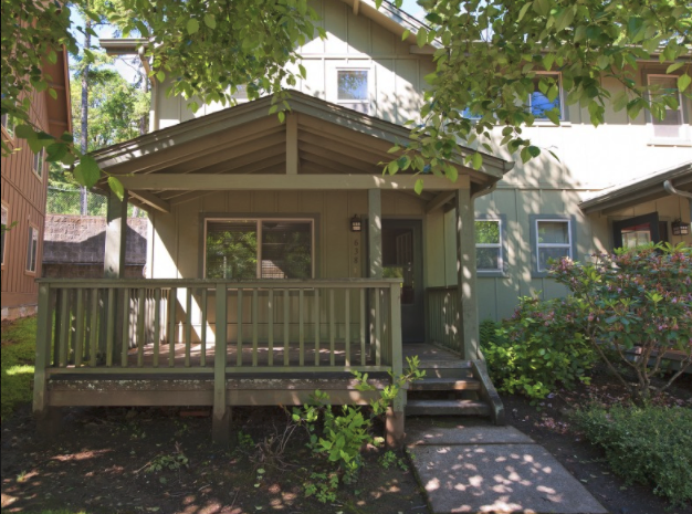 A small house with a porch and a tree in front.