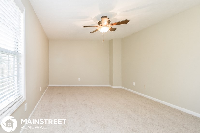 an empty living room with a ceiling fan and window