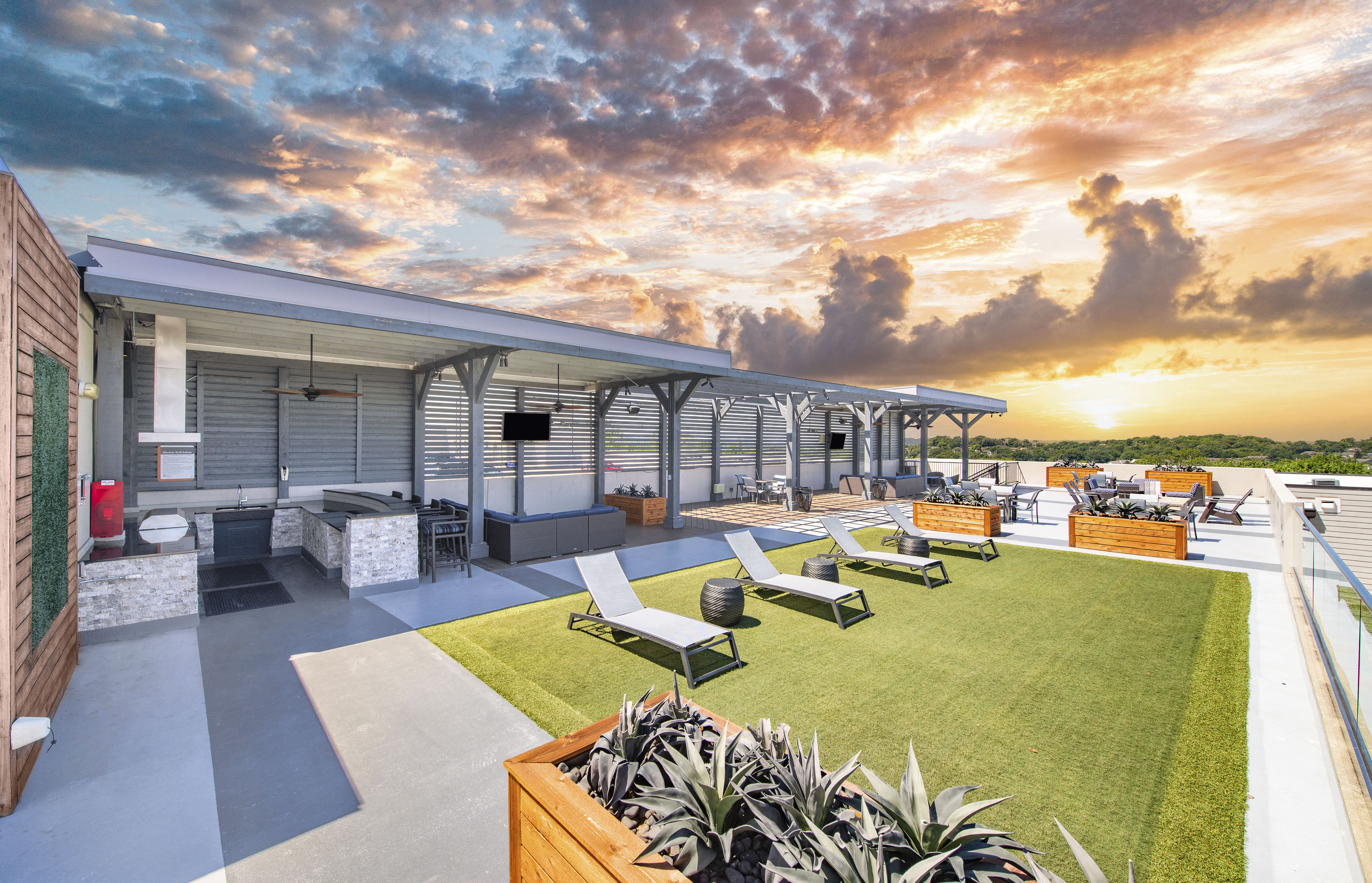 a rooftop patio with lounge chairs and a sunset in the sky
