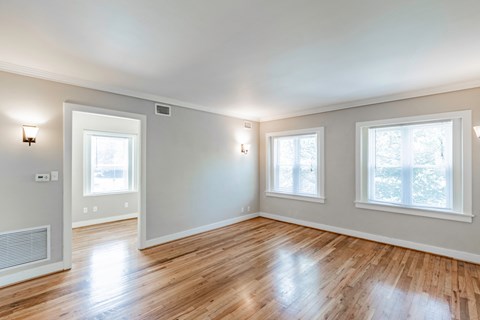an empty living room with a hard wood floor and three windows