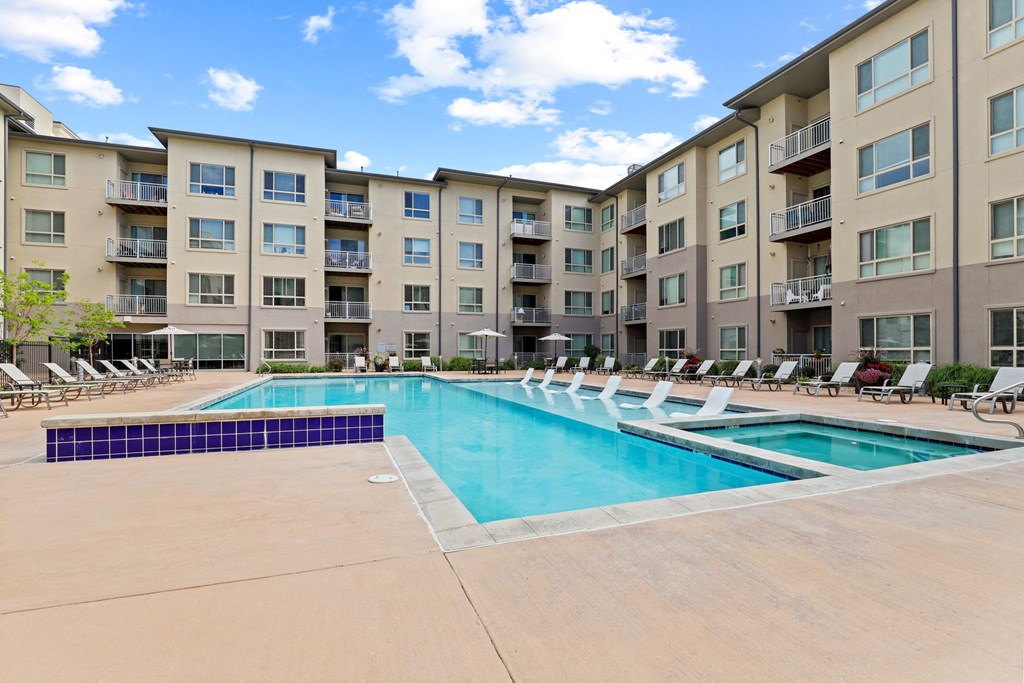 a swimming pool with lounge chairs in front of an apartment building