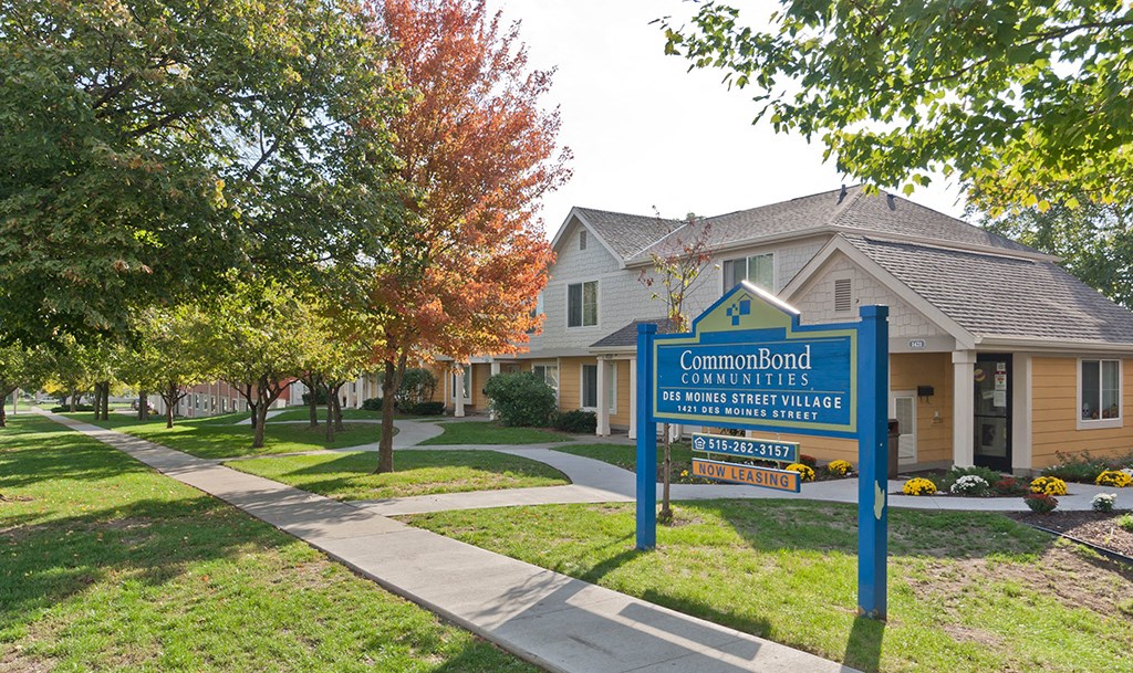 a sign in front of a house with trees and a sidewalk