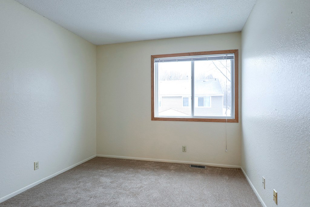 an empty bedroom with a window and carpeting