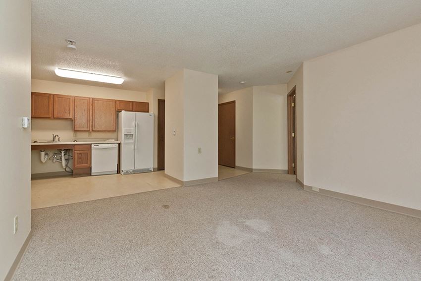 an empty living room and kitchen with a refrigerator and sink