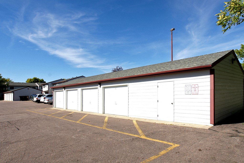a garage with white doors and a green building with a parking lot