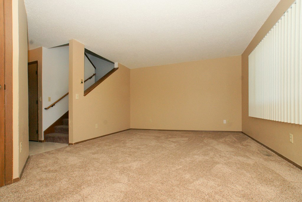 an empty living room with beige carpet and a staircase