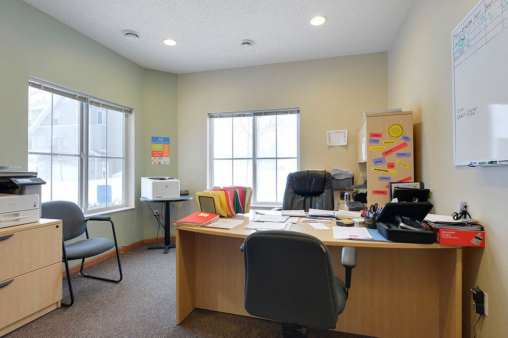 an office with a desk and chairs and two windows