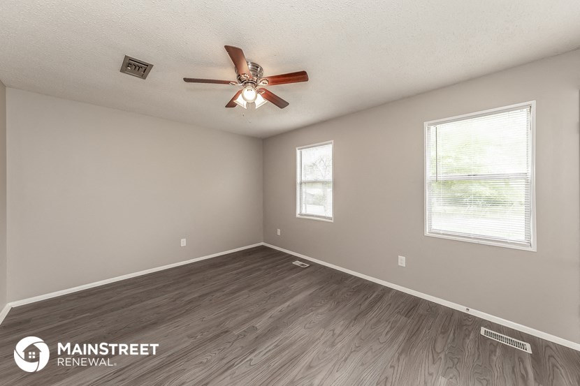 the spacious living room with wood flooring and a ceiling fan